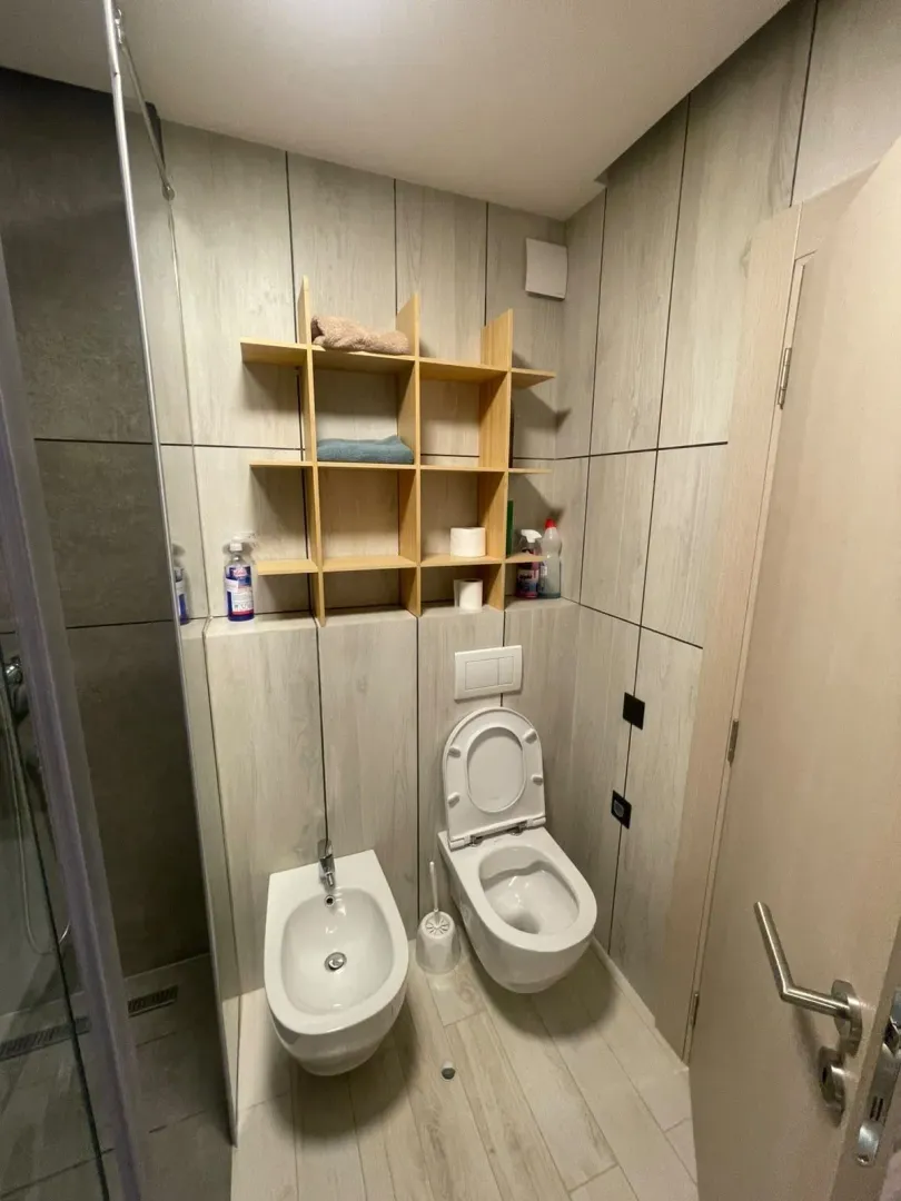 Moderno opremljeno kupatilo sa WC šoljom, bideom i drvenim policama.