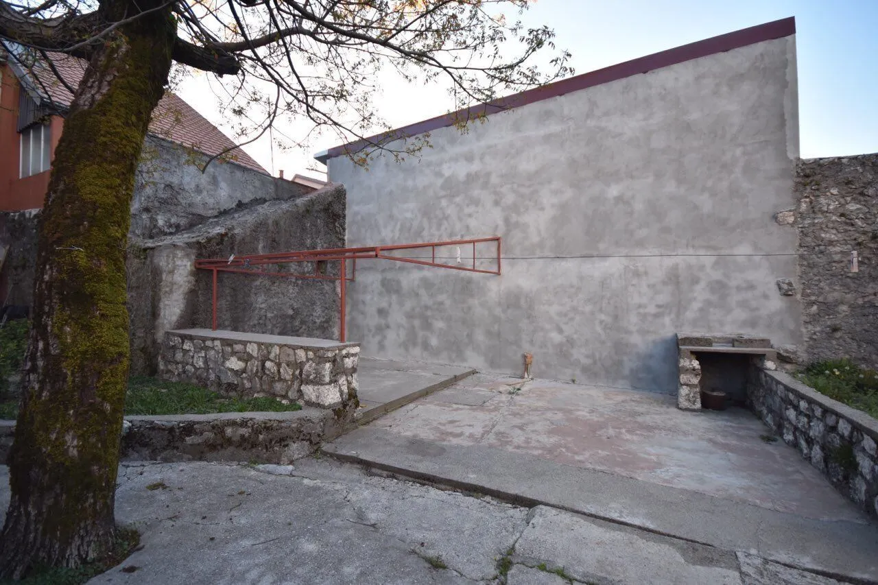 Popločano dvorište sa kamenim zidovima i drvetom pored kuće.