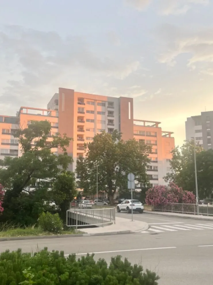 Pogled na stambenu zgradu sa okolnim zelenilom i ulicom.