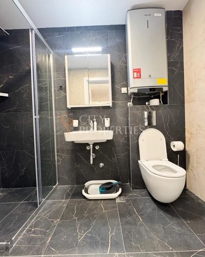 Moderne kupatilo sa tuš kabinom i crnim pločicama sa teksturom mermera.