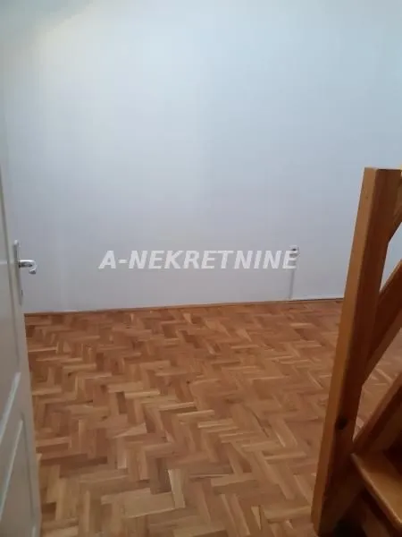 Prazna prostorija sa parketom i drvenim stepeništem.