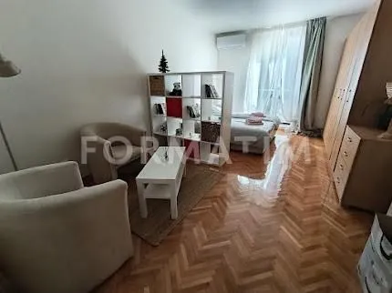 Dnevni boravak sa garniturom za sedenje, policom i drvenim podom.