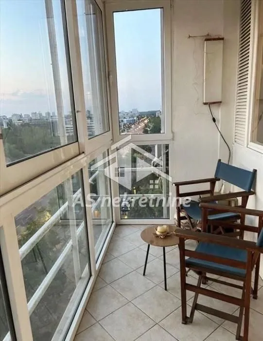 Enclosed balcony with seating furniture and a city view.