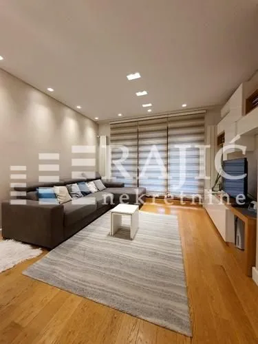 Modern living room with a sectional sofa, hardwood floors, and recessed lighting.