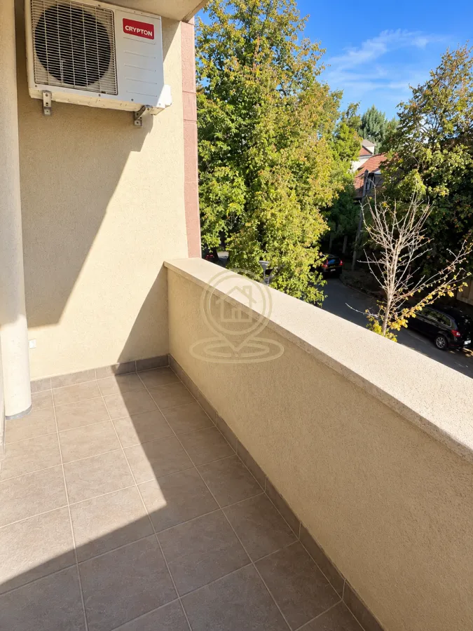 Small tiled balcony with an installed air conditioner and a view of the street and greenery.