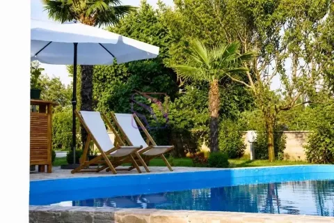 Swimming pool in the yard with sun loungers, umbrella, and greenery. - image 6