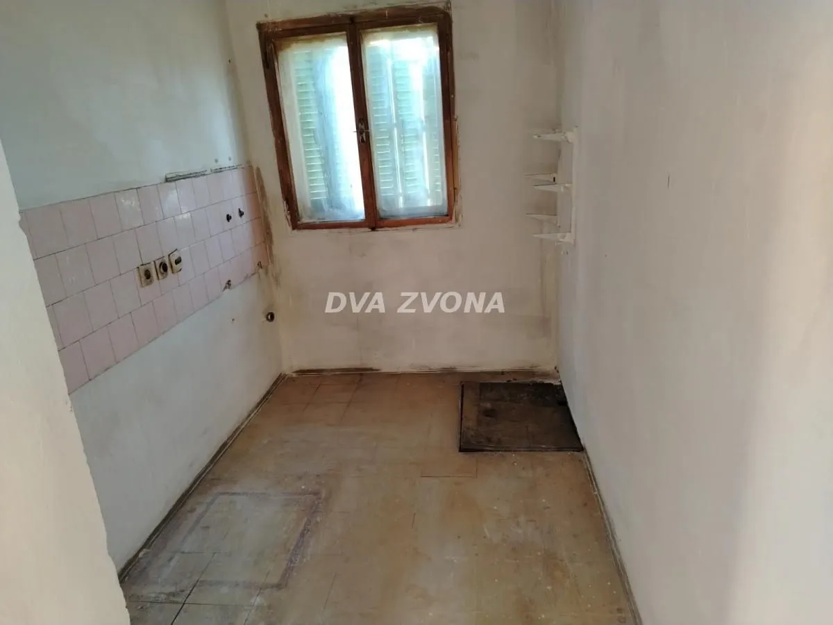 Prazna kuhinja sa starim pločicama i prozorom, spremna za renoviranje.