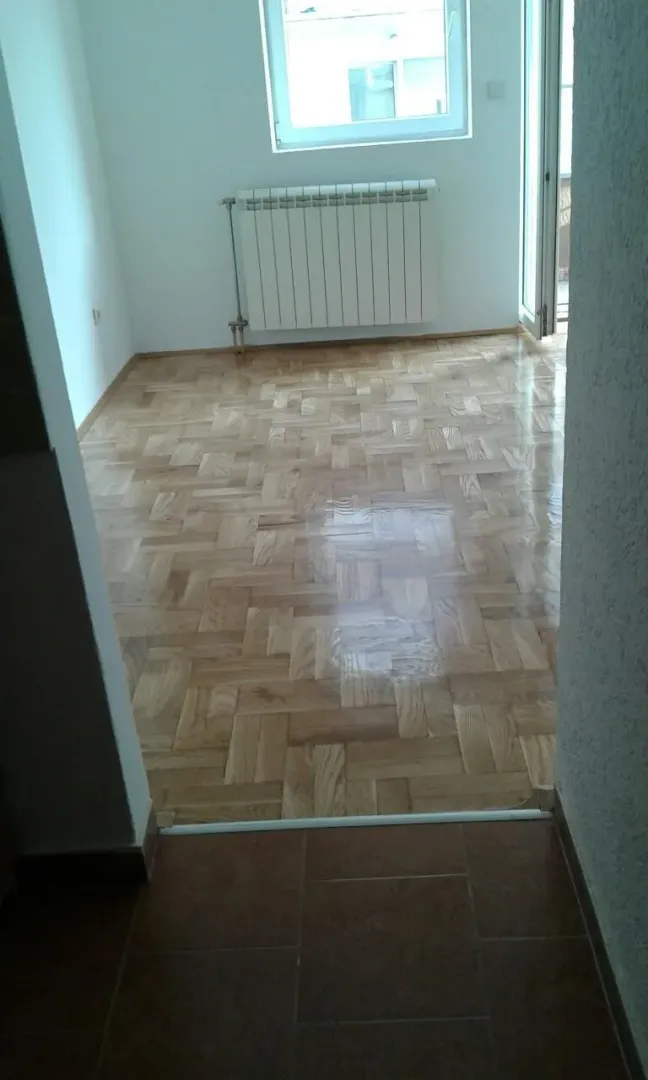 Prazna soba sa parketom i radijatorom.