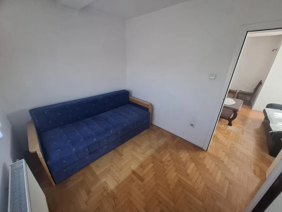 Manja soba sa plavim kaučem i parketom na podu.