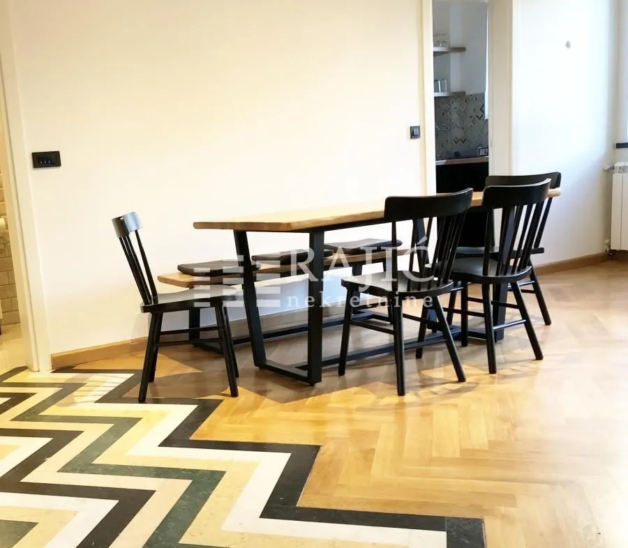 Dining area with a wooden table and black chairs on parquet flooring.