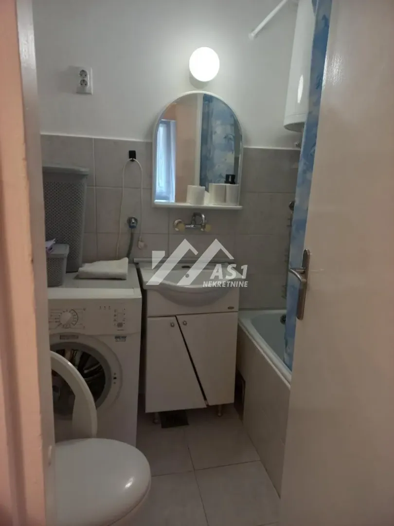 Pogled na kupatilo sa umivaonikom, kadom, WC šoljom i veš mašinom.
