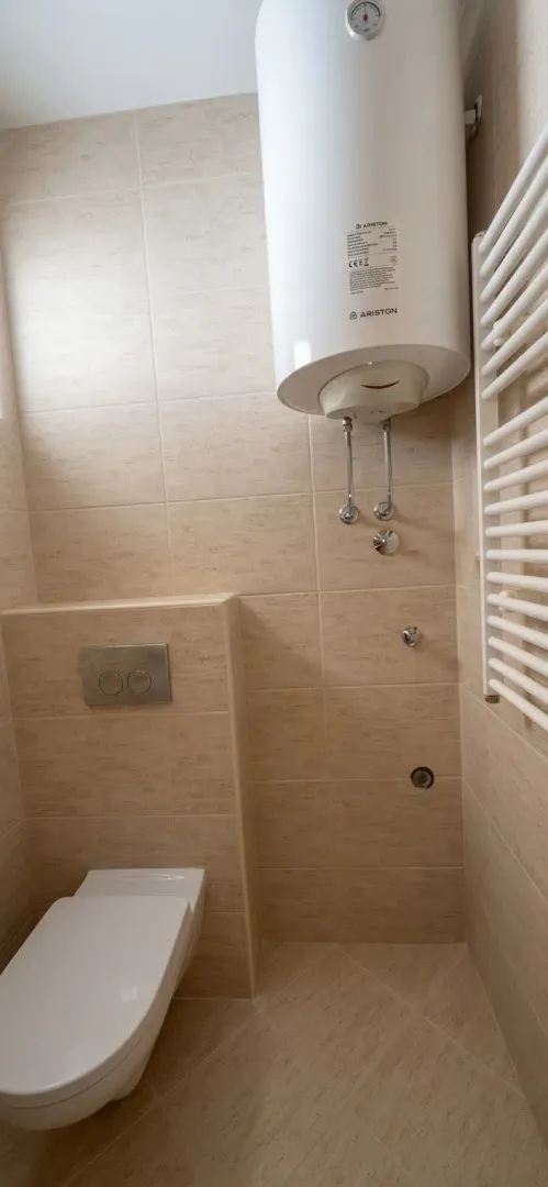 Pogled na kupatilo sa wc šoljom, bojlerom i pločicama.