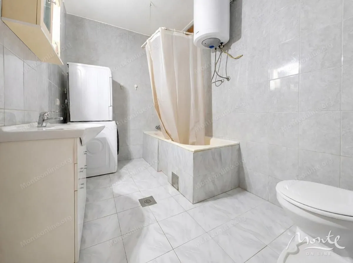 Kupatilo obloženo sivim pločicama sa kadom, umivaonikom i WC šoljom.