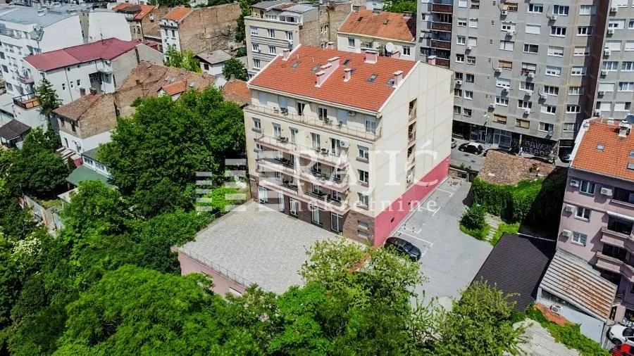 Aerial view of an apartment building with surrounding park and parking lot.