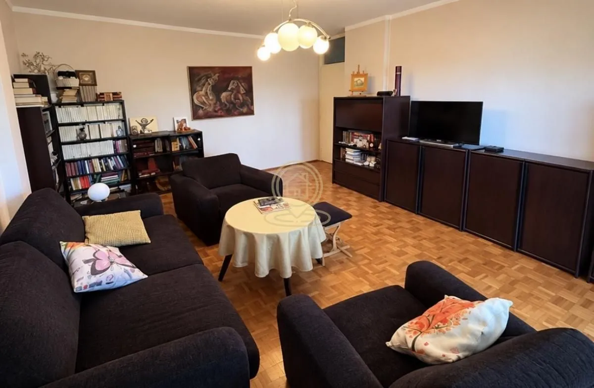 Living room furnished with seating arrangements, bookshelves, and a television.