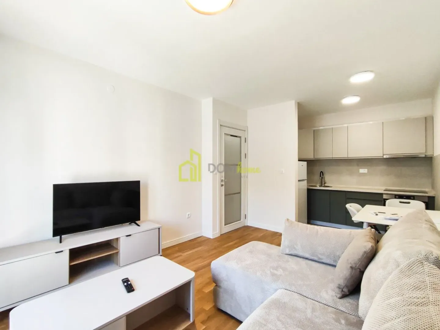 Living room with sofa, TV and kitchen in the background.