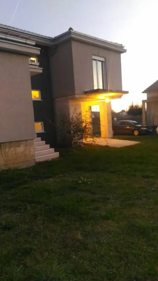 Exterior view of a modern house with an illuminated entrance and lawn at dusk.