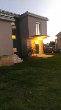 Exterior view of a modern house with an illuminated entrance and lawn at dusk. - image 3