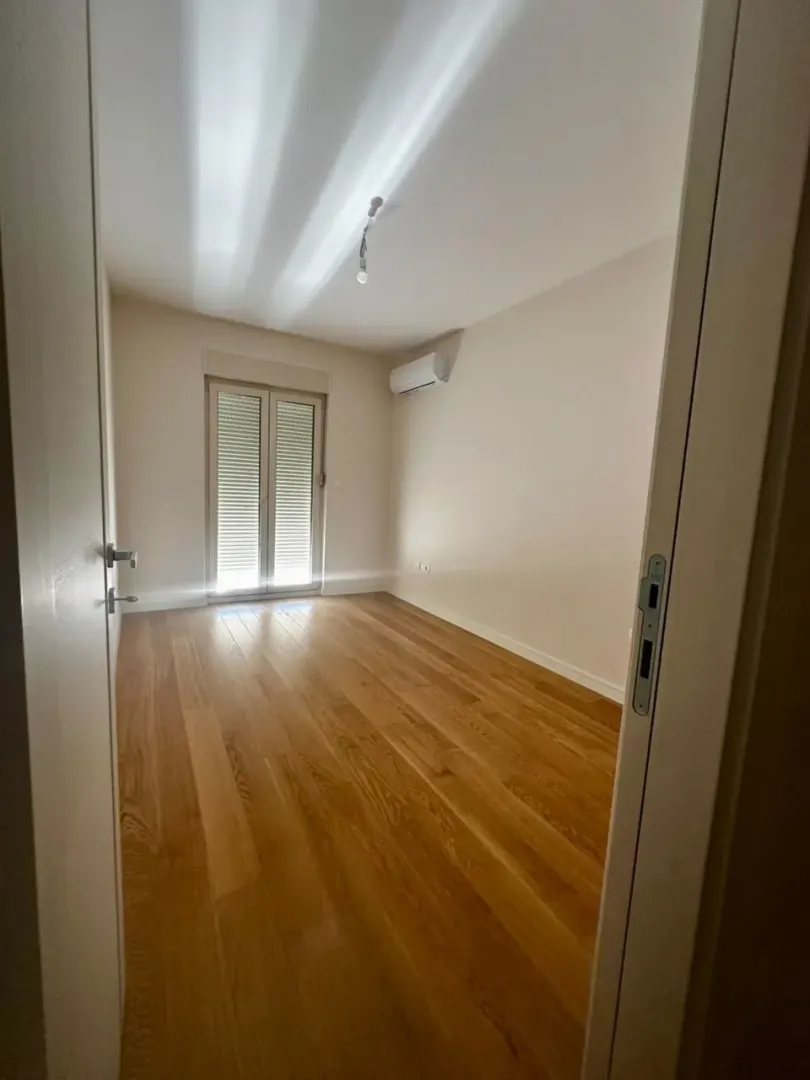Empty room with wooden flooring and balcony doors.