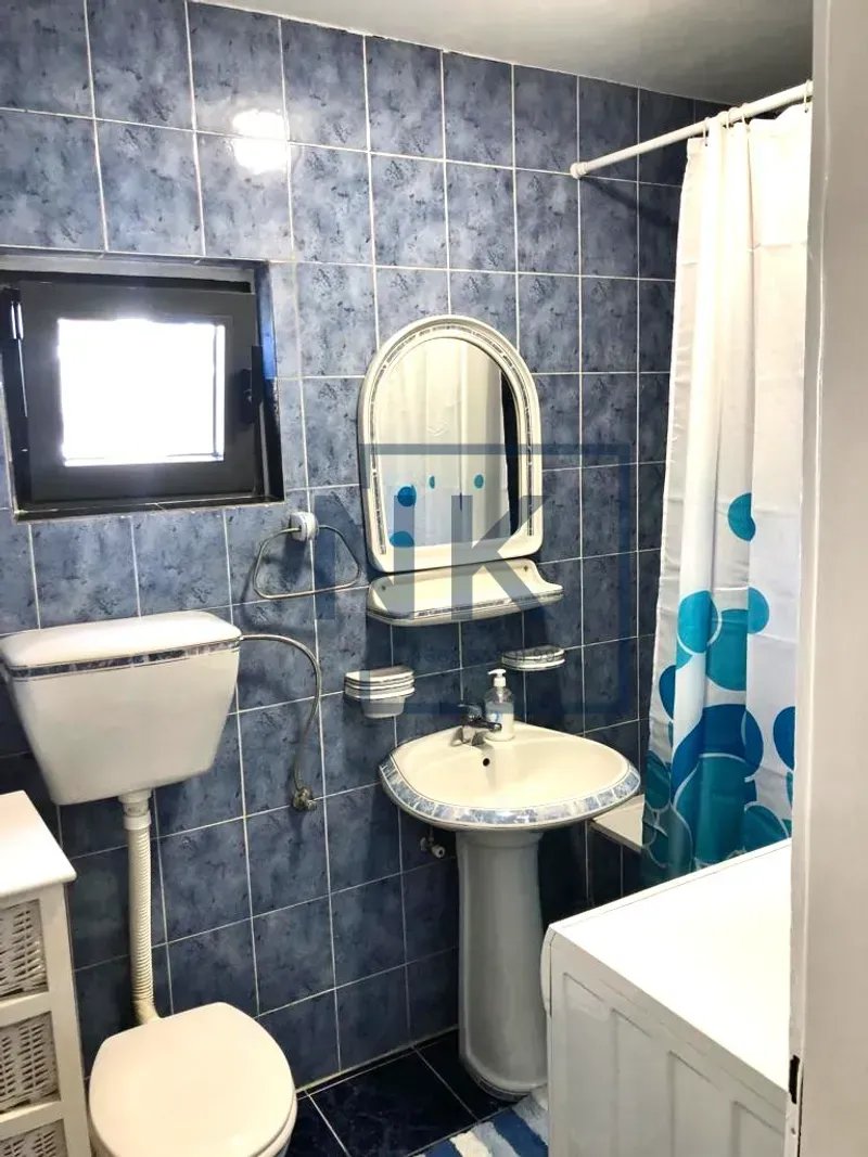 Bathroom lined with blue tiles, featuring a toilet, a sink, and a bathtub with a curtain.