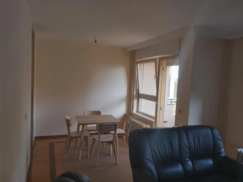 Dnevna soba sa trpezarijskim stolom, stolicama i crnom kožnom garniturom.