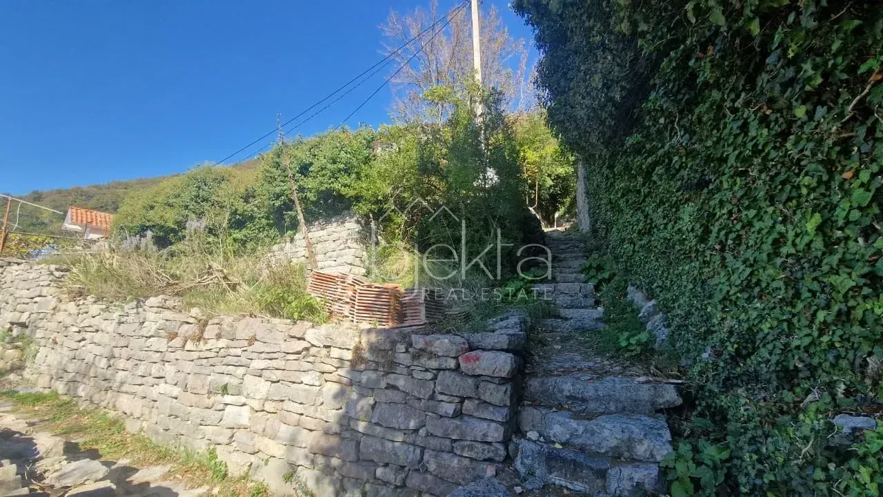 Kamene stepenice vode pored starog zida i zelenila u dvorištu.