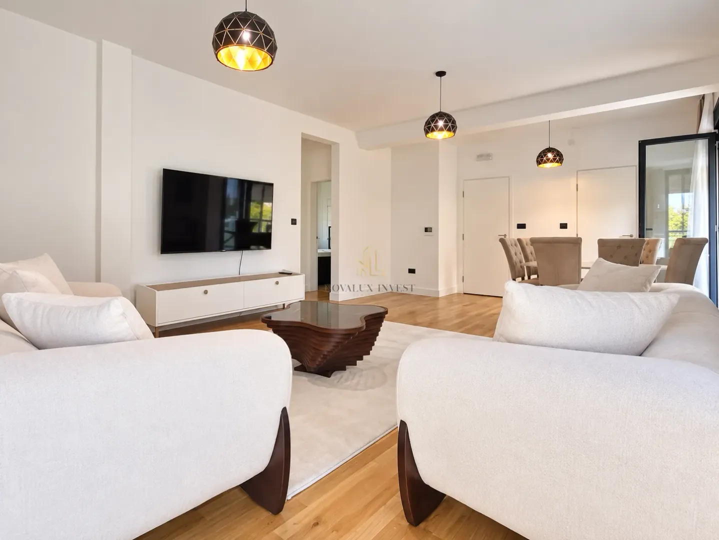 Spacious living room with sofa set, TV and dining area in the background.