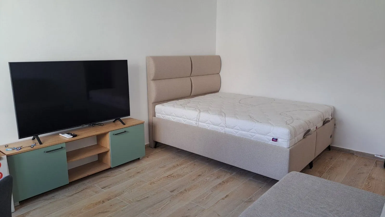 Spavaća soba sa bračnim krevetom, komodom i televizorom.