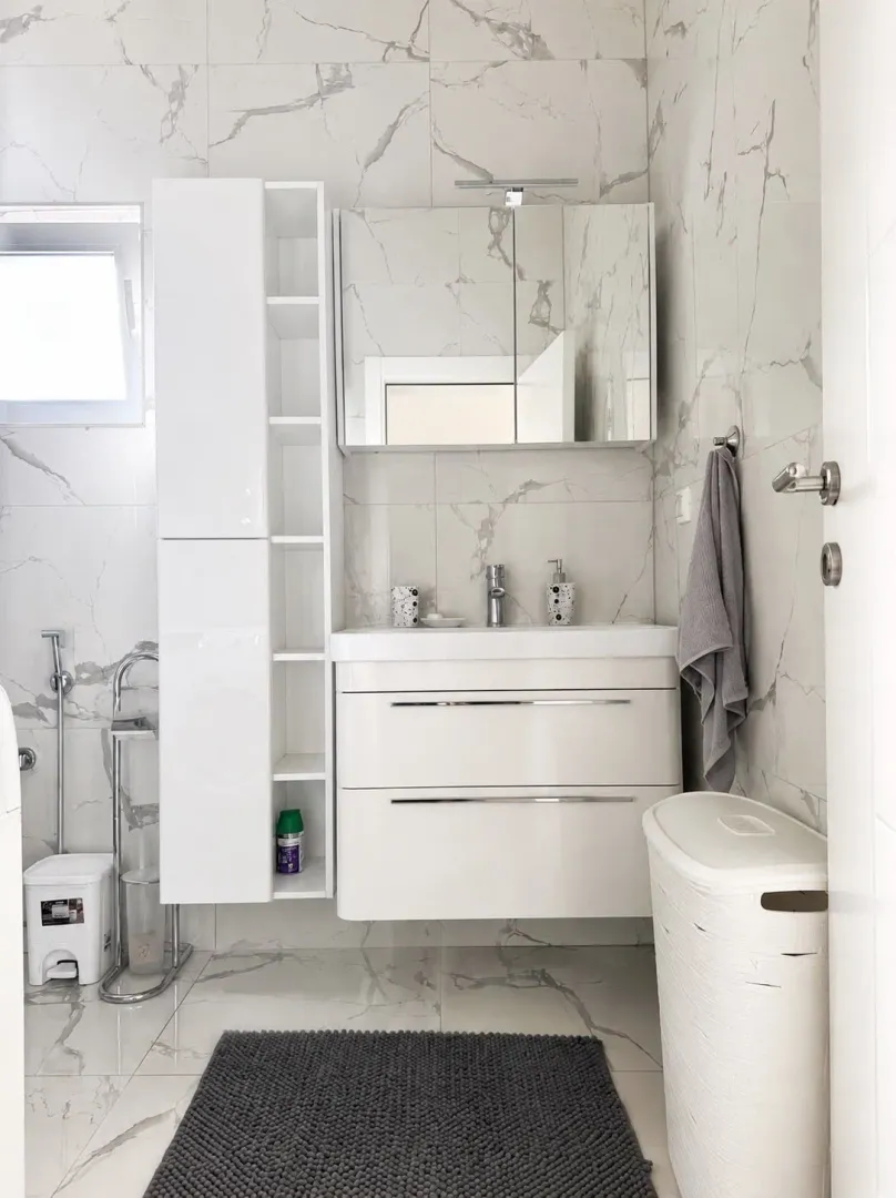 Modernly equipped bathroom with white furniture and marble tiles.