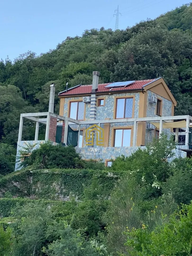 Eksterijer kuće sa kamenom fasadom i terasom okružene zelenilom.