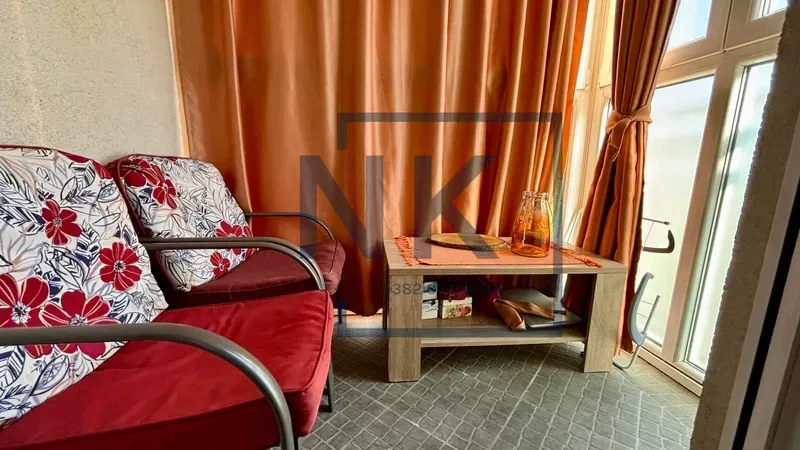 Enclosed balcony with armchairs, a small coffee table, and orange curtains.