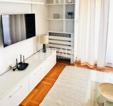 Bright living room with white furniture, television, and hardwood flooring. - image 13