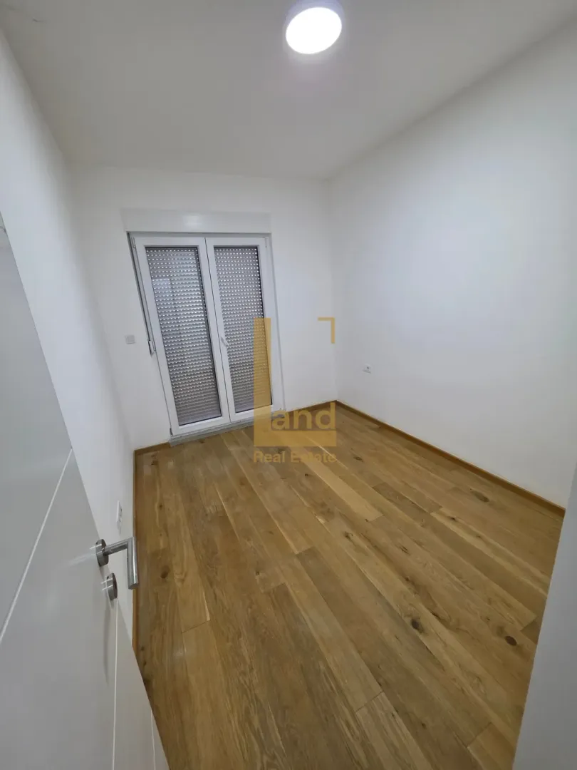 Prazna soba sa drvenim podom i balkonskim vratima.