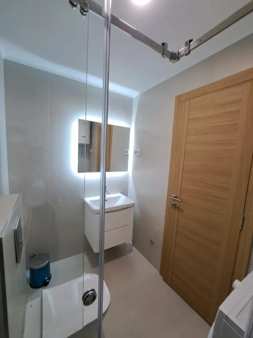 Modernly equipped bathroom with a washbasin, illuminated mirror, and a shower cabin.