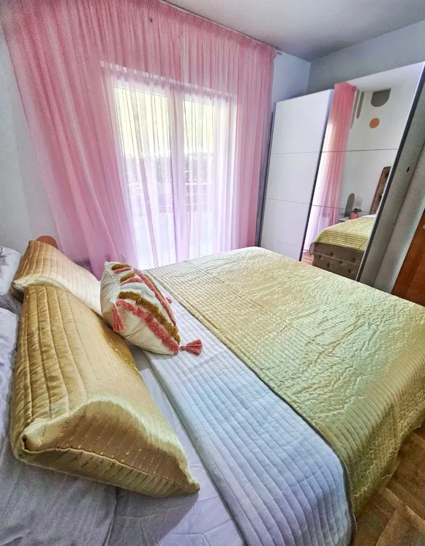 Furnished bedroom with a large double bed, wardrobe, and pink curtains.