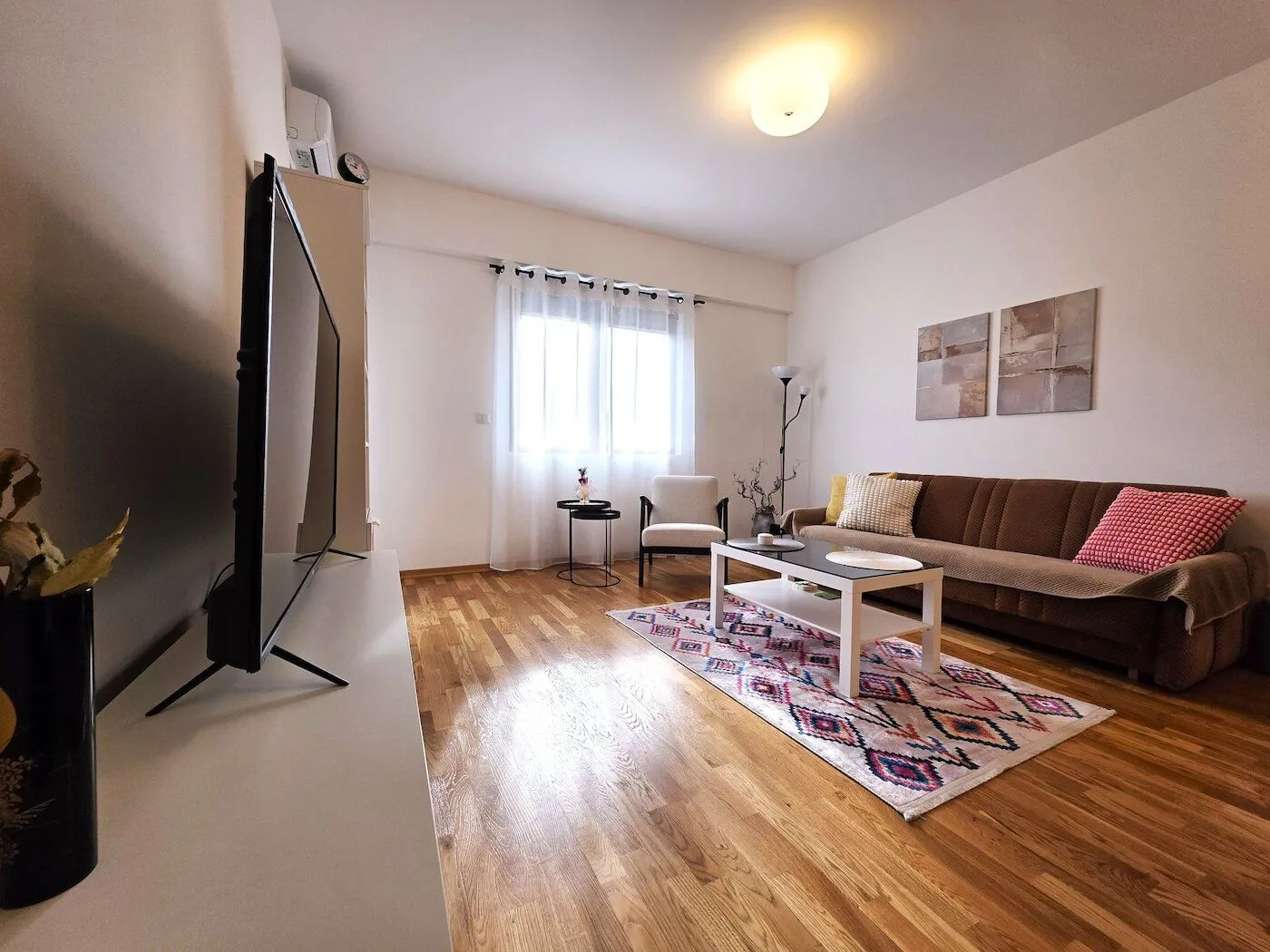 Living room with a sofa, TV, and wooden flooring.