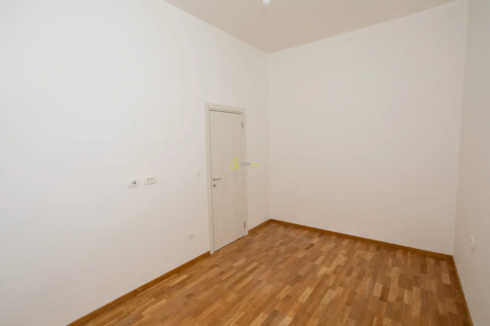 Prazna soba sa bijelim zidovima i drvenim podom.