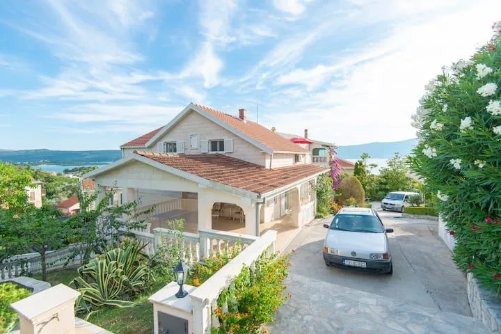 Pogled na spoljašnjost kuće sa dvorištem, terasom i parkiranim automobilom.