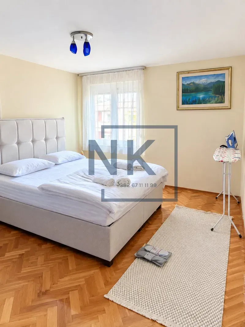 Furnished bedroom with a double bed, window, and parquet flooring.