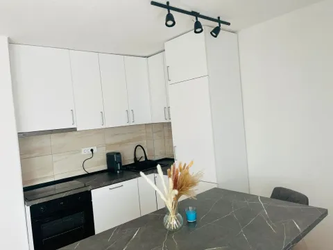 Moderna bijela kuhinja sa tamnom radnom površinom i trpezarijskim stolom. - image 6