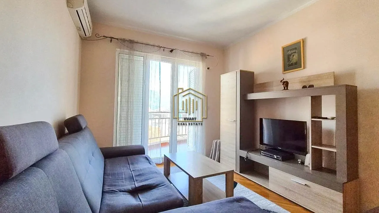 Dnevna soba sa garniturom, TV komodom i izlazom na terasu.
