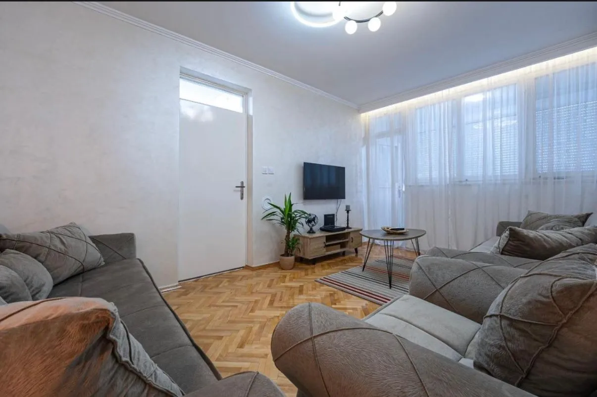 Furnished living room with a sofa set, TV, and parquet flooring.