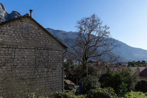 Pogled na kamenu kuću i dvorište sa drvećem u pozadini. - image 6