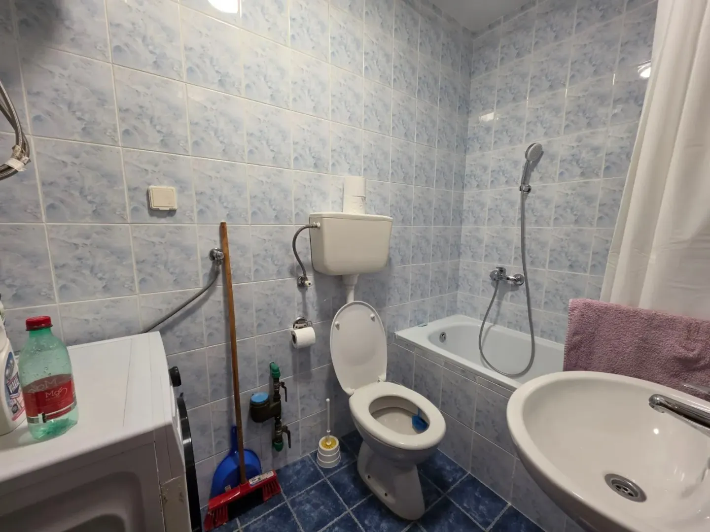 Smaller bathroom with blue-toned tiles, bathtub, and toilet.