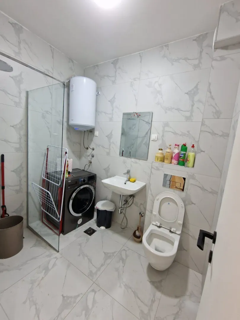 Bathroom with light tiles, a washing machine, and a shower.