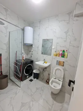 Bathroom with light tiles, a washing machine, and a shower. - image 9