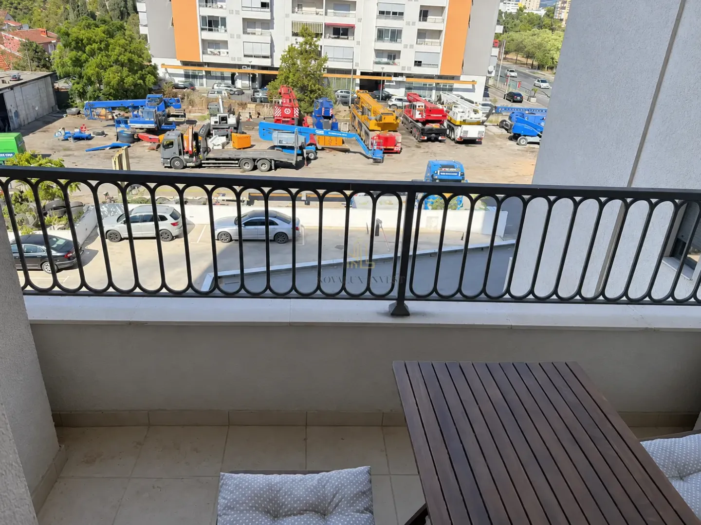 Nenamešten balkon sa pogledom na parking i građevinsku mehanizaciju.