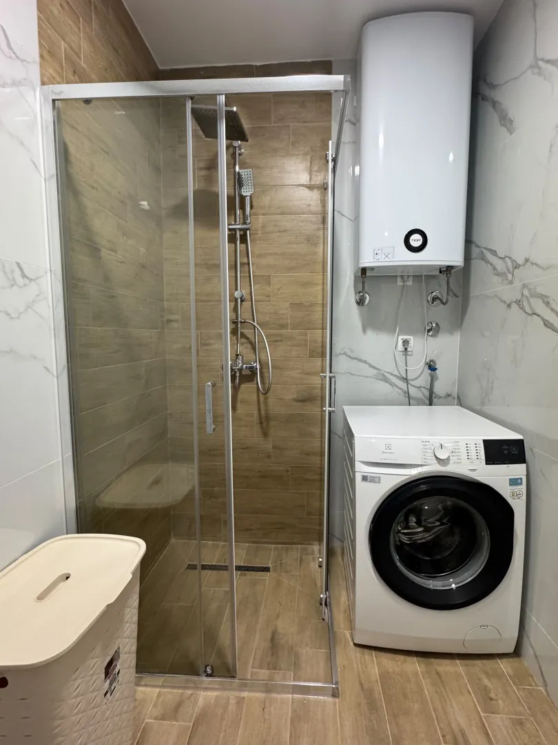 Modernly equipped bathroom with a walk-in shower, water heater, and washing machine.