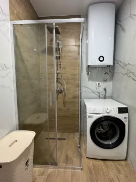 Modernly equipped bathroom with a walk-in shower, water heater, and washing machine. - image 6