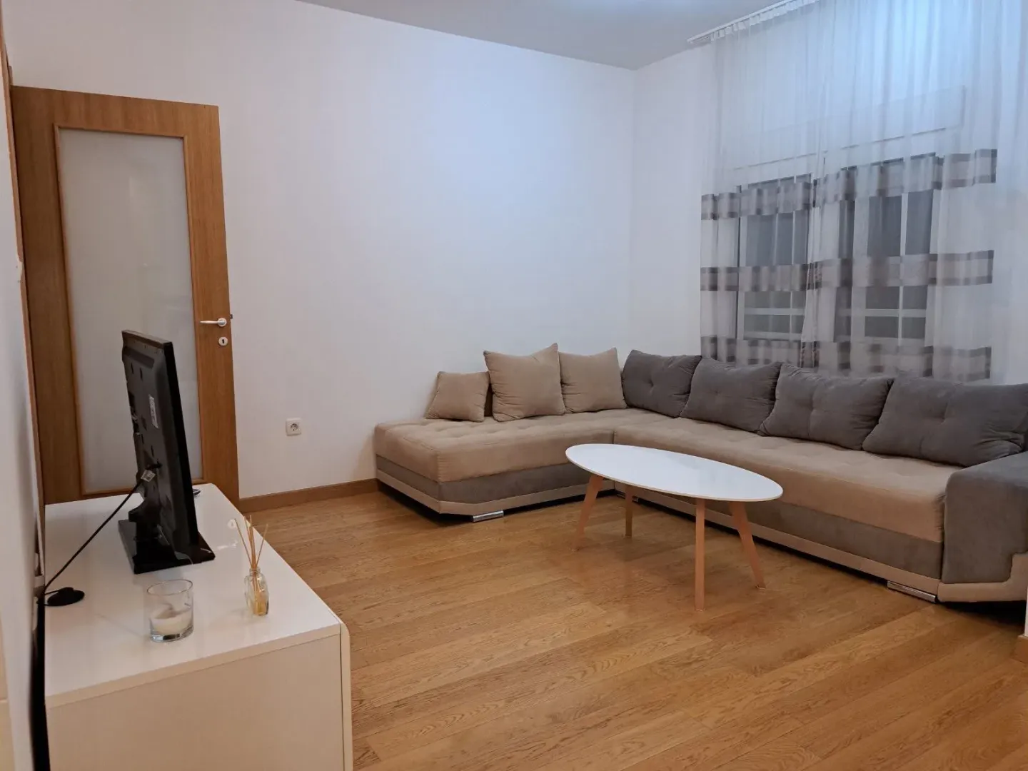 Furnished living room with a sectional sofa, TV, and wooden flooring.
